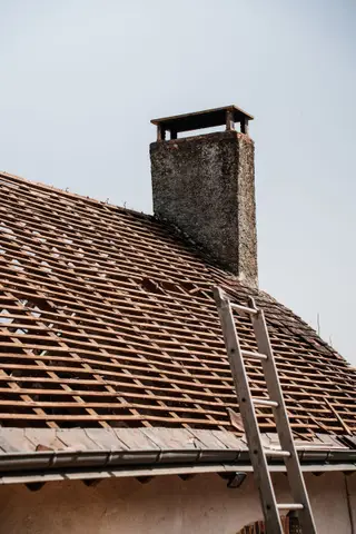 Roof stripped down to its battens beside a chimney