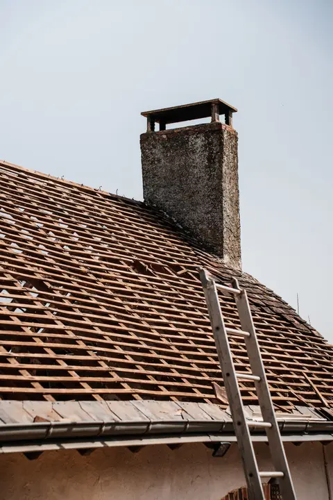 Roof stripped down to its battens beside a chimney